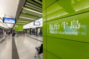 Green wall panel with South Horizons sign in English and Chinese at a busy subway platform passengers wait for trains in the background