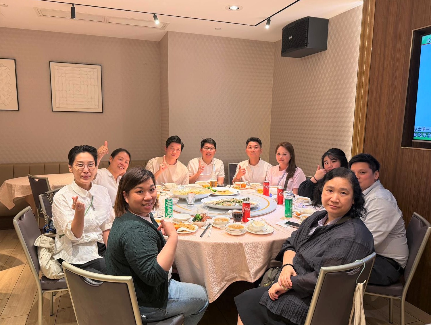 Group of friends and colleagues around a round dining table, posing and giving thumbs up in a restaurant.