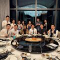 Group of colleagues in formal wear posing with thumbs up around a round dining table centered by a seafood platter