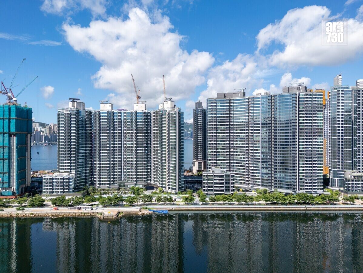 Row of glassy apartment towers along a riverfront with construction cranes and a blue sky behind them, AM730 watermark in the top-right corner