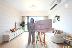 Woman in a gray suit stands beside a large Mori Signature Series promotional sign in a bright modern living room