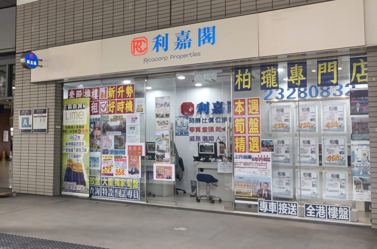 Storefront for a real estate agency with Chinese signage and large glass windows covered in property listings and colorful posters.