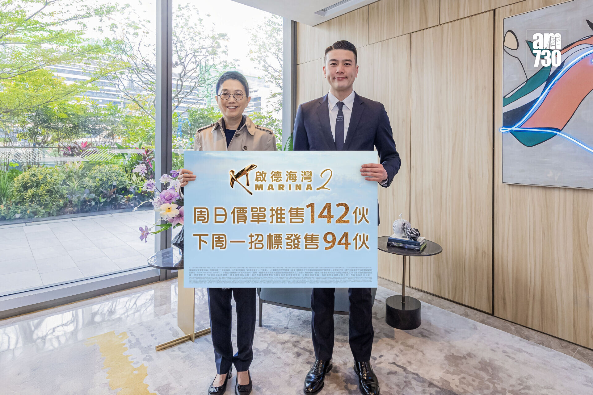 Two people in business attire pose indoors, holding a large sign with Chinese text and the word 'MARINA'.