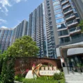 Tall glass front residential towers with curved balconies against a blue sky with greenery in the foreground and a Marina sign at the entrance