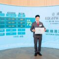 Man in a gray suit holding a certificate in front of a blue display wall for a real estate event HighwoodVictoria Cove Area