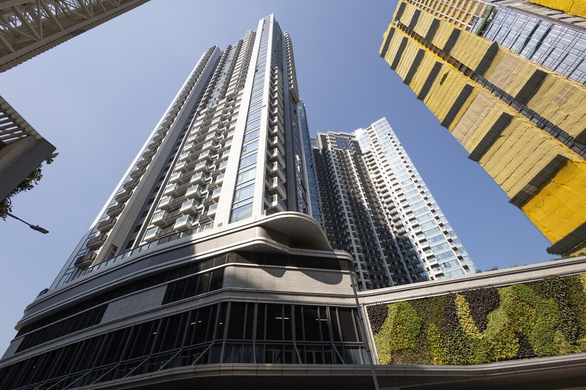 Low-angle view of tall modern skyscrapers against a clear blue sky, with a green wall feature at the base.