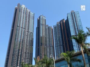 Cluster of tall glass clad office towers reaches into a clear blue sky with palm trees in the foreground and an AM730 logo in the top right corner