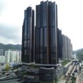 Tall modern residential skyscraper cluster rising above a city with hills in the background and a rail line nearby