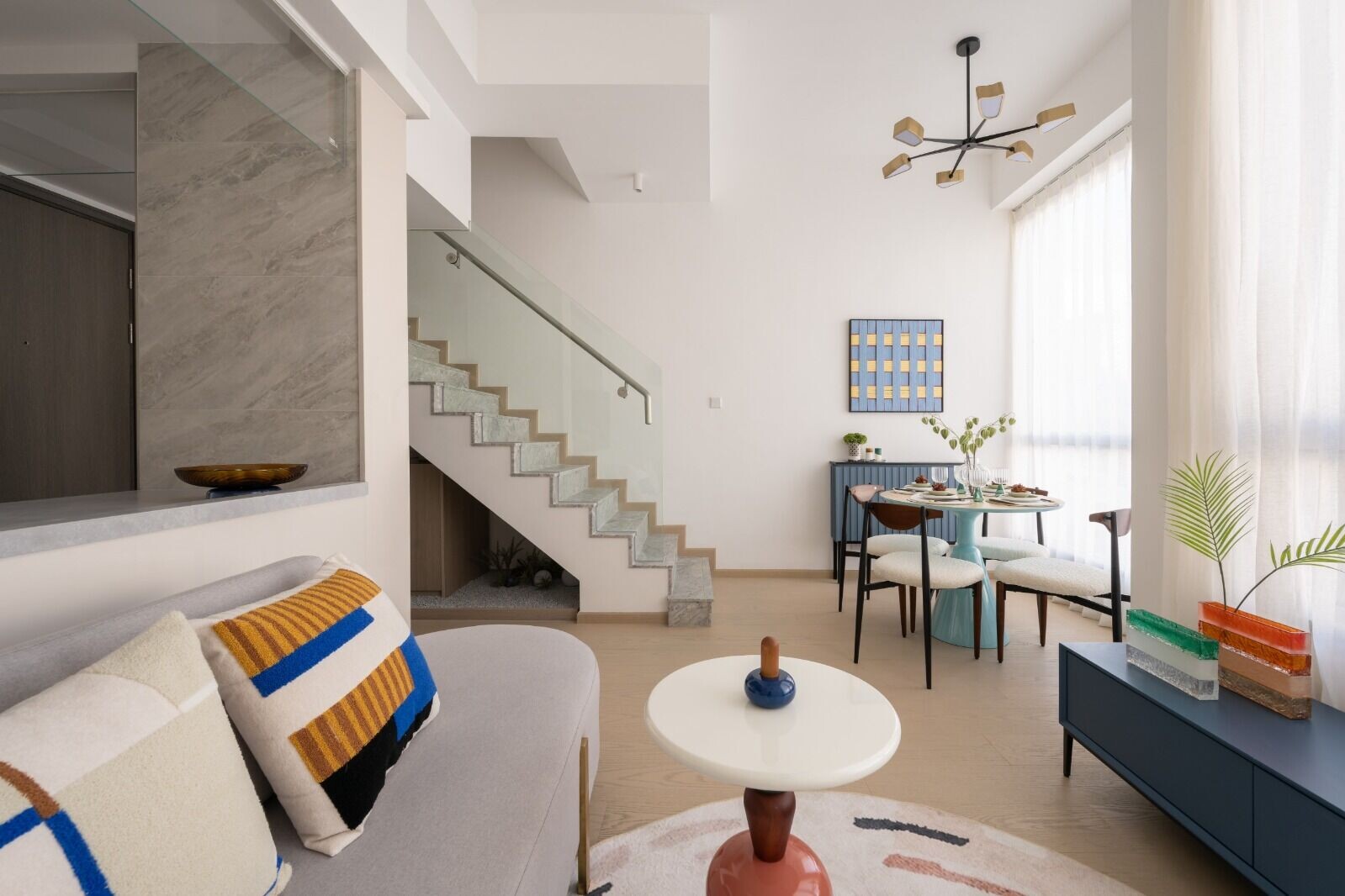 Bright open livingdining area with a curved gray sofa colorful striped cushions and a white round coffee table in the foreground