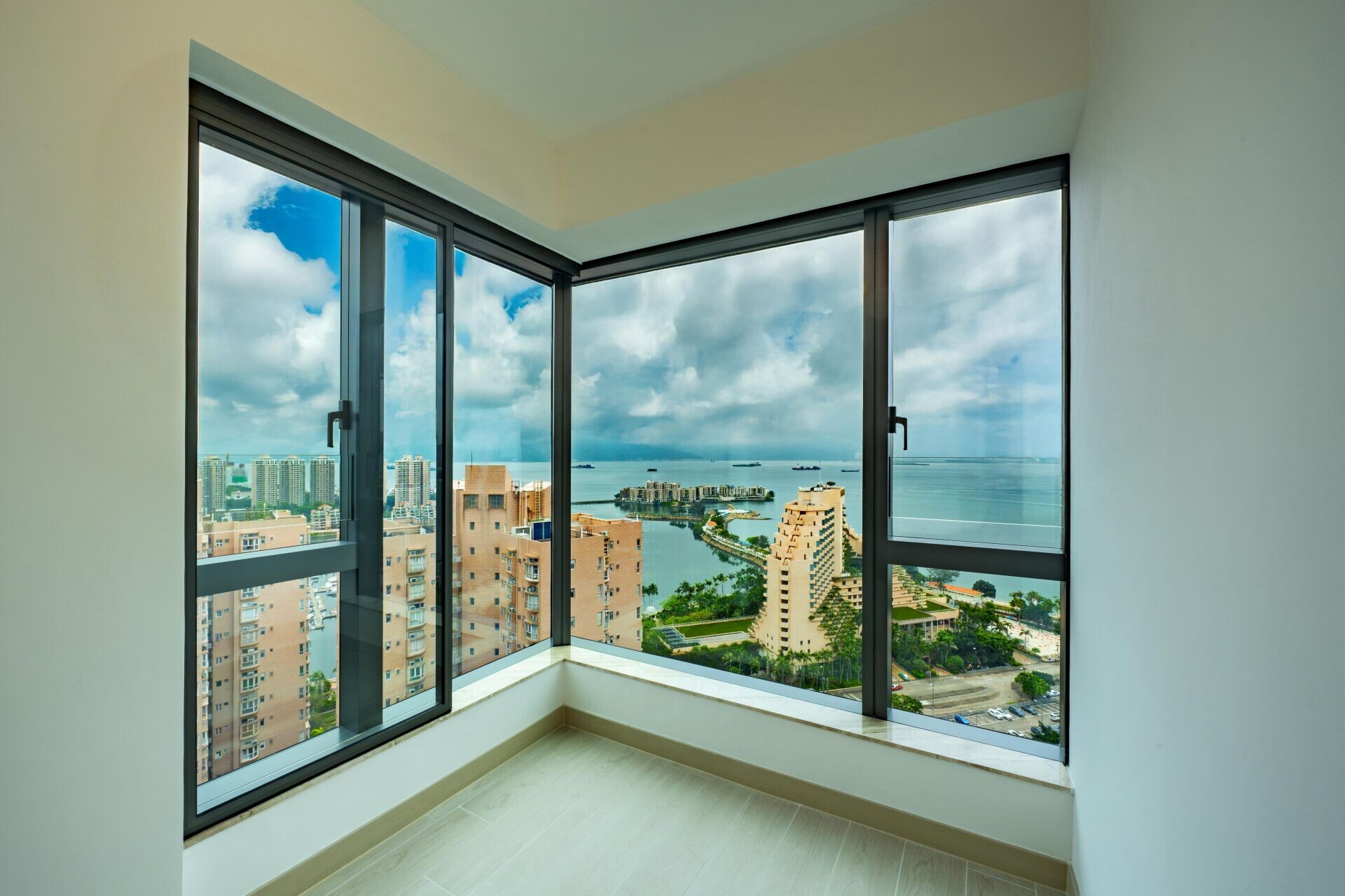 Corner room with floor-to-ceiling windows overlooking a coastal city and the sea beyond.