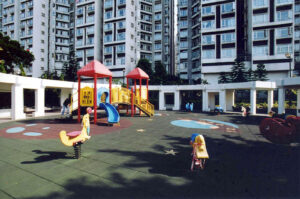 Colorful childrens playground with red roofed structures yellow slides and climbing equipment set against tall apartment buildings in a residential complex