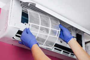 Hands wearing blue gloves insert a filter into a wall mounted air conditioner unit