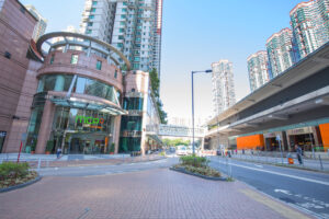 Wide city street with a glass fronted mall entrance curved metal structure and tall residential towers under a blue sky