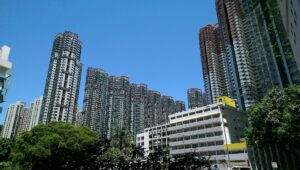 Cluster of tall grey residential towers under a clear blue sky with green trees in the foreground
