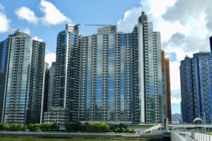 61b10b29853eb93d87447bb8dc9ab3737796bd~mv2 | 利嘉閣地產有限公司 Row of tall glass residential towers along a waterfront under a blue sky with scattered clouds A promenade with trees runs along the water in the foreground