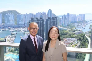 Two smiling professionals posing on a balcony with a city skyline and marina in the background