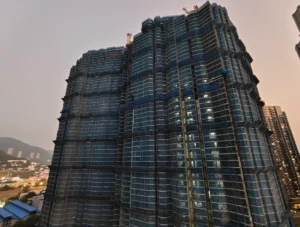 Tall glass clad skyscraper under construction with cranes at the top city lights below at dusk