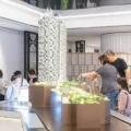 People gather around a large detailed scale model of a tall residential tower in a showroom or exhibition space examining the model closely