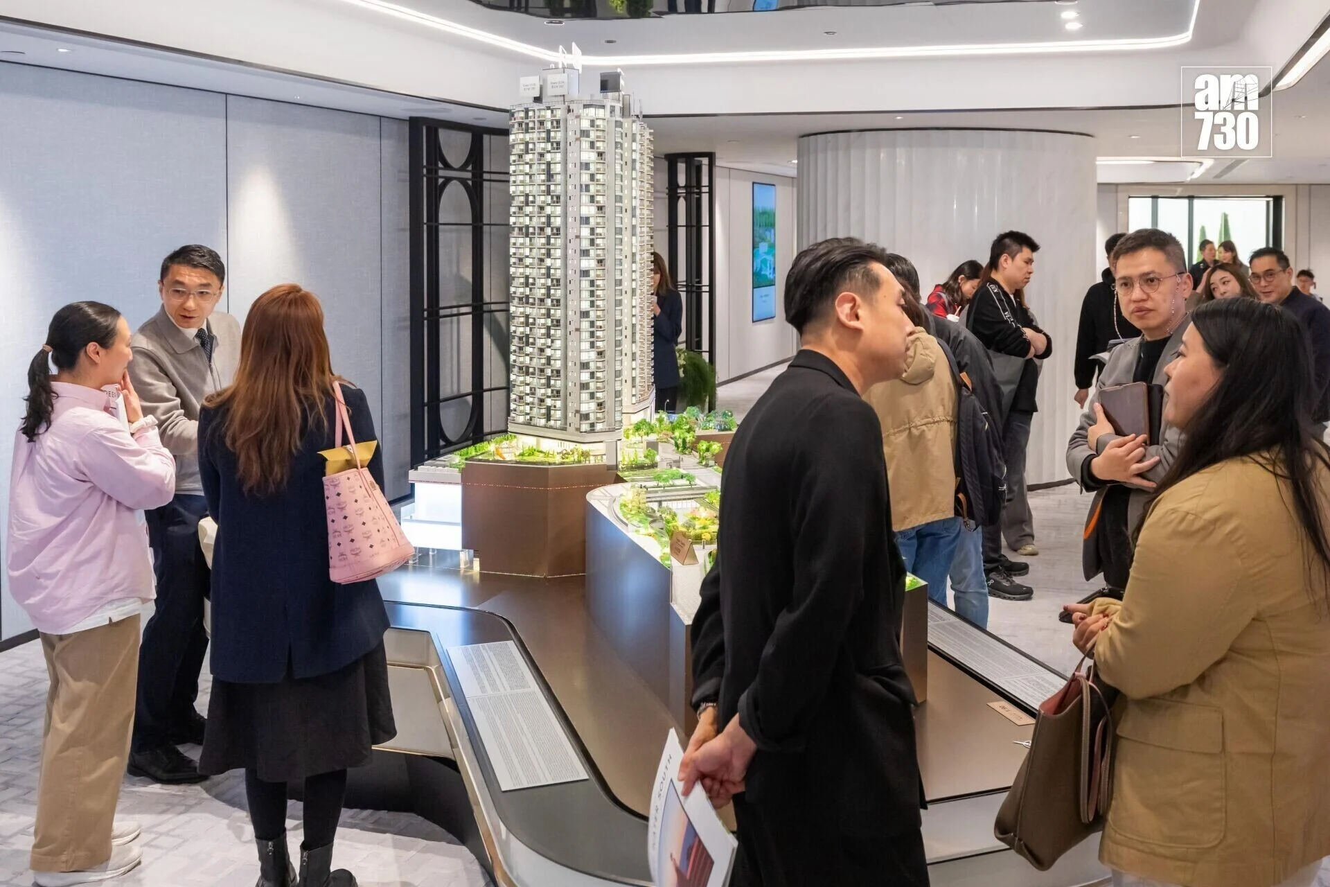 Group of people in a modern showroom admiring a detailed scale model of a high-rise building.