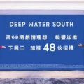 Two people stand on either side of a large blue banner reading DEEP WATER SOUTH with Chinese text beneath it posing for a photo