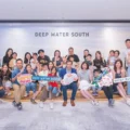 Large group photo of families and friends posing together at a Deep Water South event holding colorful signs and props