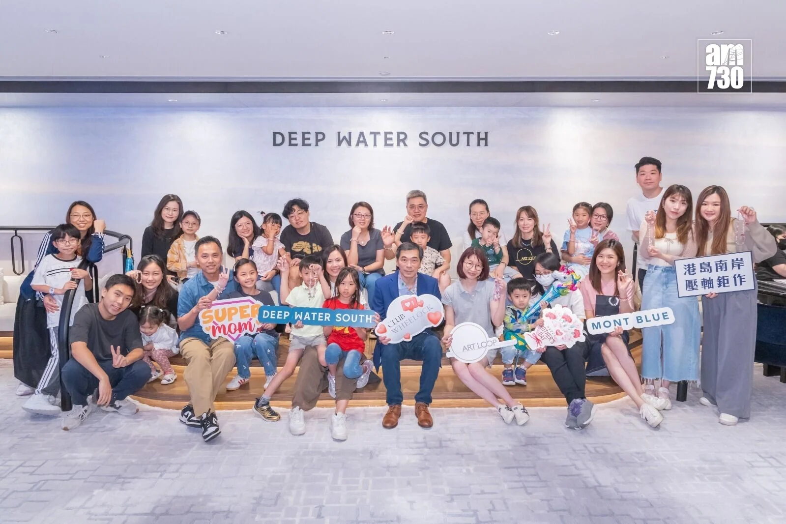 Large group photo of families and friends posing together at a Deep Water South event, holding colorful signs and props.