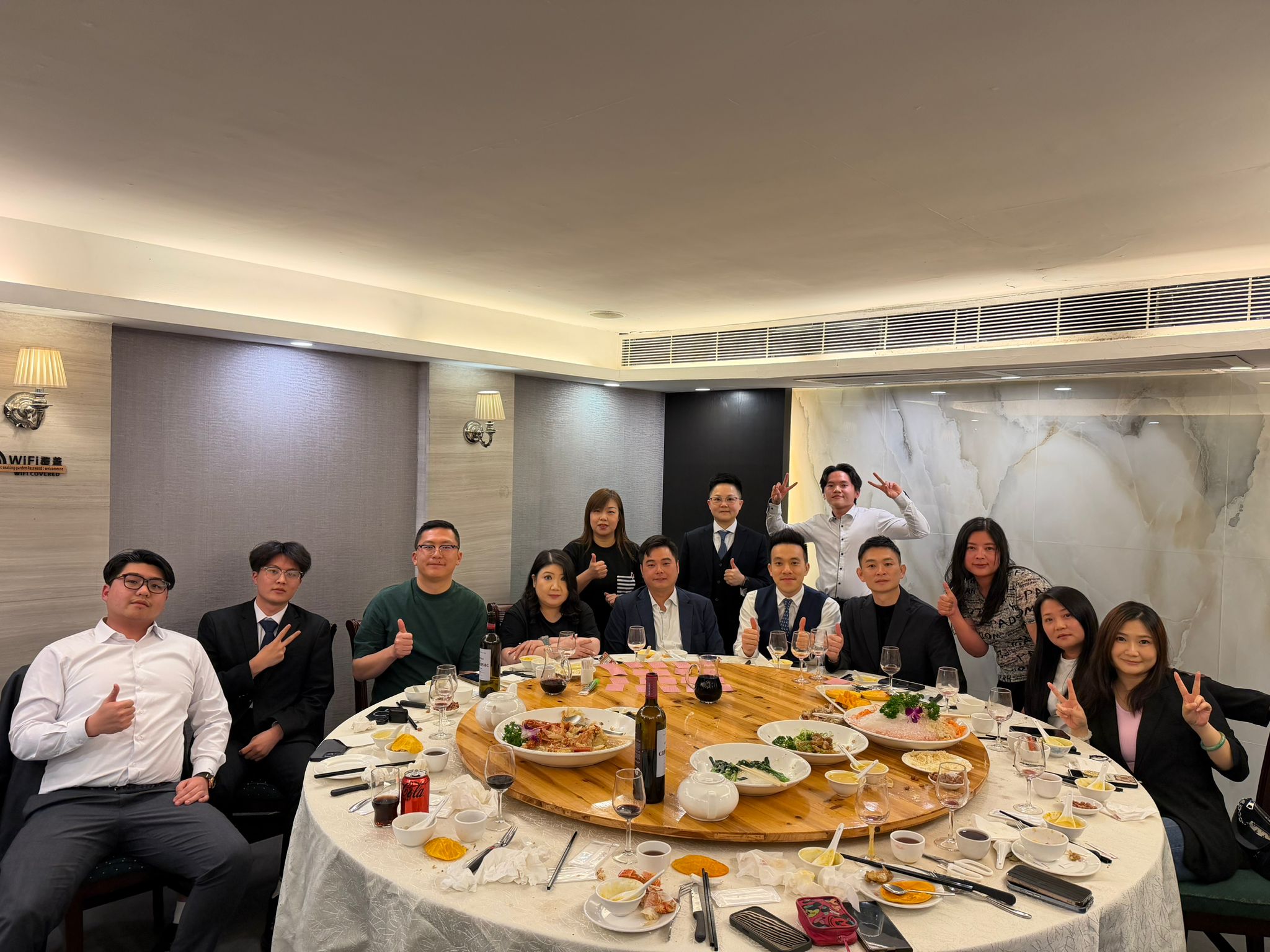 Group of coworkers at a banquet table, posing with thumbs up after a meal in a formal restaurant setting.