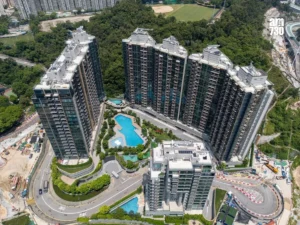 Aerial view of a modern U shaped cluster of high rise residential towers surrounding a central pool area and landscaped courtyards with a curved road and construction nearby