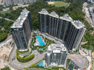 Aerial view of a U shaped cluster of high rise apartment towers surrounding a kidney shaped blue swimming pool and landscaped grounds