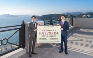 Two men in business suits stand on a seaside terrace holding a large sign with Chinese text ocean and mountains in the background