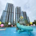 Tall glass residential towers with a turquoise waterslide in a pool area surrounded by colorful balloons and amenities