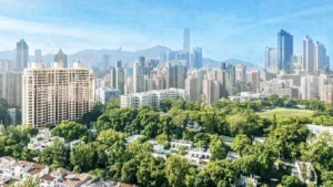 Aerial view of a dense city skyline with tall skyscrapers and a large green park in the foreground under a blue sky mountains in the distance