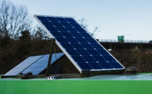Blue solar panels tilted on a green rooftop outdoors with trees in the background