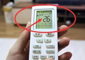White handheld remote control with a digital display showing 26°C held in a persons hand