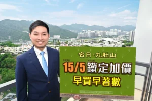 Asian man in a navy suit on a balcony holding a large green sign with Chinese text city skyline and mountains in the background