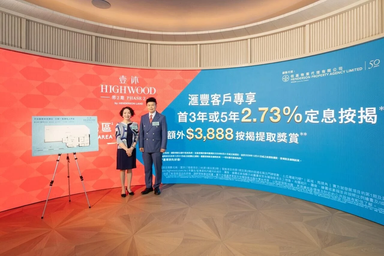Two professionals pose in front of a red‑blue promotional backdrop for Highwood Phase 2, with an easel displaying a floor plan on the left.