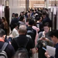 Crowded elevator lobby with dozens of people standing in a narrow hallway between elevator doors