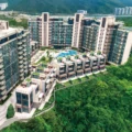 Aerial view of a surrounding luxury apartment complex with glass facades central pool and green hills in the background AM730 watermark in the top right corner