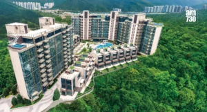 Aerial view of a surrounding luxury apartment complex with glass facades central pool and green hills in the background AM730 watermark in the top right corner