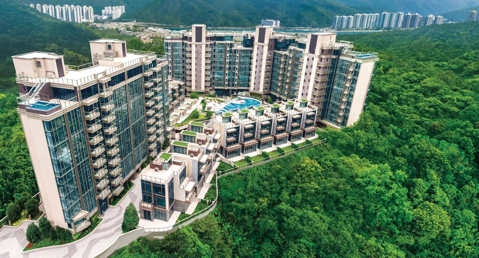 Modern hillside apartment complex with glass façades, a central pool, and surrounding green forest.