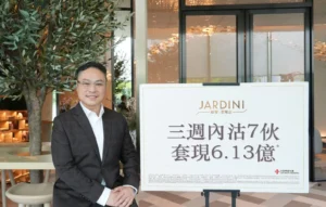 Man in a dark suit smiles beside a large white sign with the JARDINI logo and Chinese text in a bright lobby with plants behind him
