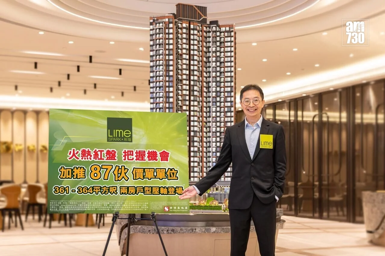 Asian man in a dark suit with a yellow Lime badge stands beside a tall high-rise model and a green advertisement board in a showroom.