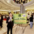 Smiling man in a suit gives a thumbs up beside a large green sign announcing 5700 units sold at an indoor real estate event Crowds are gathered in the background