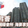 Tall high rise residential towers under a blue sky with a promotional Chinese banner and a logo in the top left advertising a premium seaview club facilities
