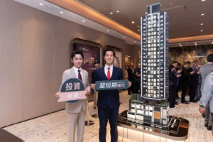 Two men in suits pose at a real estate showroom holding Chinese signs beside a tall architectural tower model