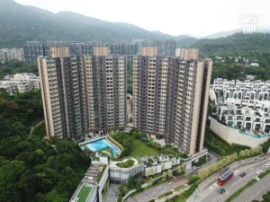 Aerial view of a U shaped cluster of high rise apartment buildings with a central pool and landscaping set against hills in the background