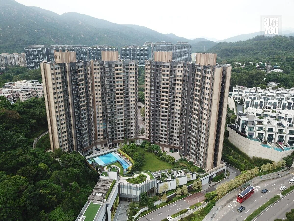 Aerial view of a U-shaped cluster of high-rise apartment buildings with a central pool and landscaping, set against hills in the background.