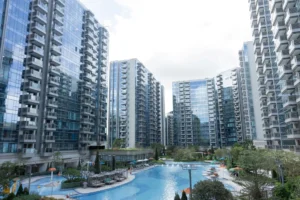 Modern glass apartment towers surround a curving outdoor pool area with lounge chairs and umbrellas