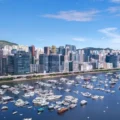 Harbor filled with moored yachts and speedboats with a dense city skyline along the waterfront under a blue sky