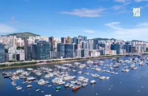 Harbor filled with moored yachts and speedboats with a dense city skyline along the waterfront under a blue sky